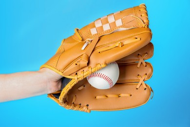 Photo of Baseball player holding ball with catcher's mitt on light blue background, closeup. Sports game