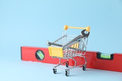 Photo of Shopping cart with different construction tools on light blue background, space for text