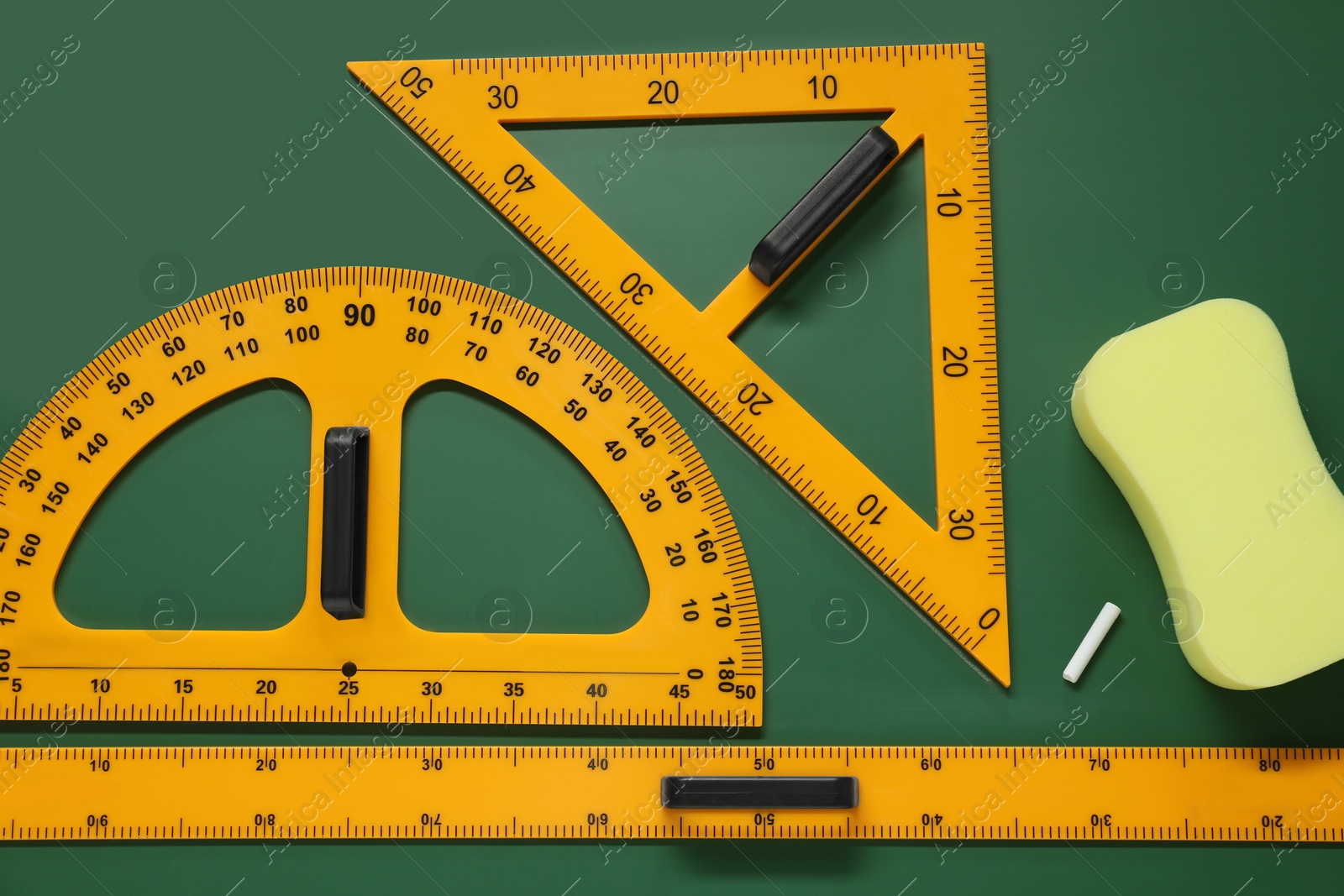 Photo of Protractor, triangle, ruler and sponge on green chalkboard, flat lay