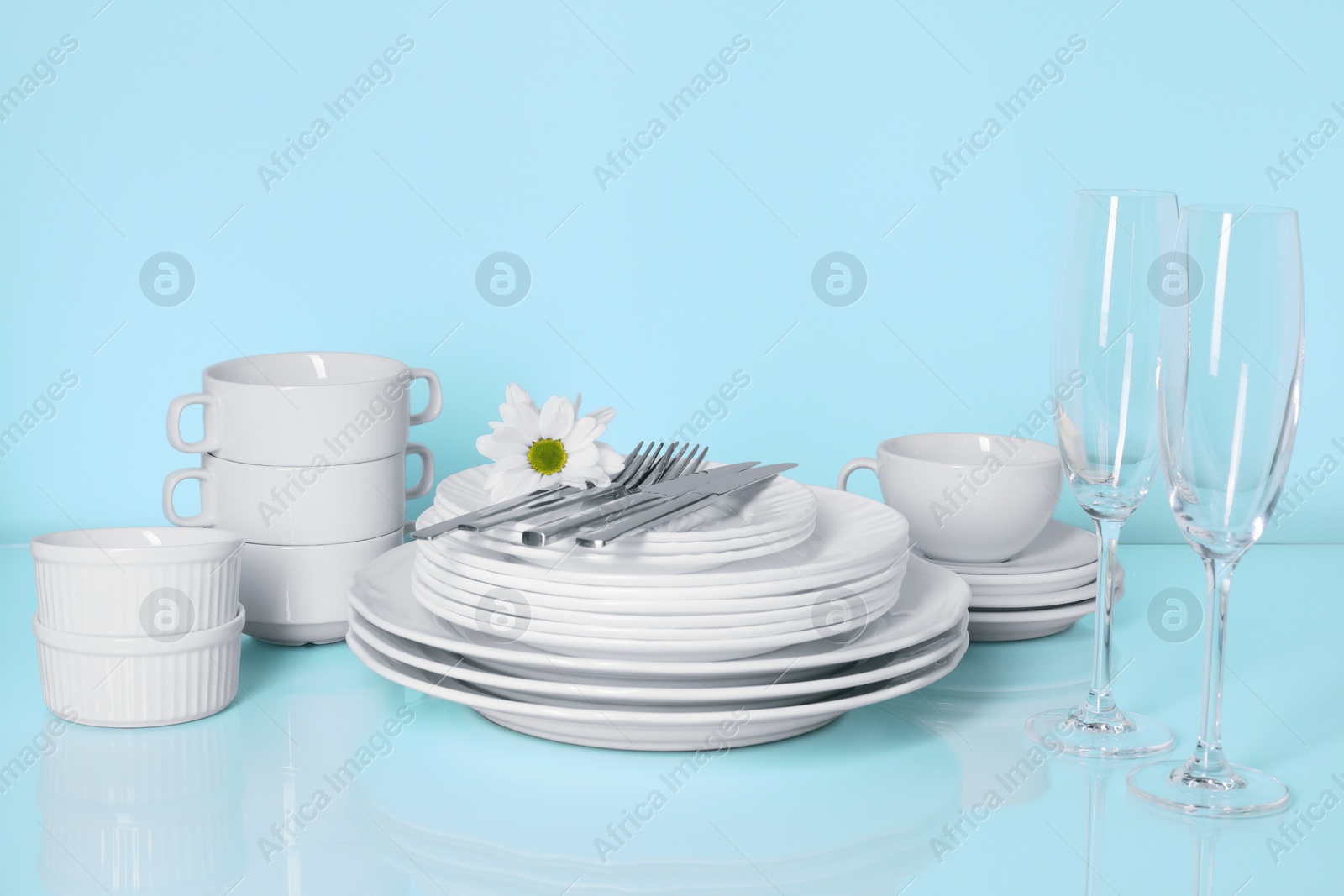 Photo of Set of clean dishes, glasses and cutlery on light blue table