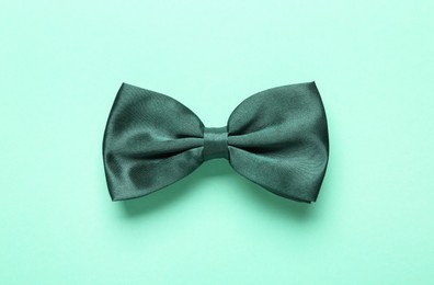 Stylish satin bow tie on light green background, top view