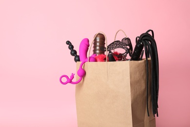 Photo of Paper shopping bag with different sex toys on pink background. Space for text