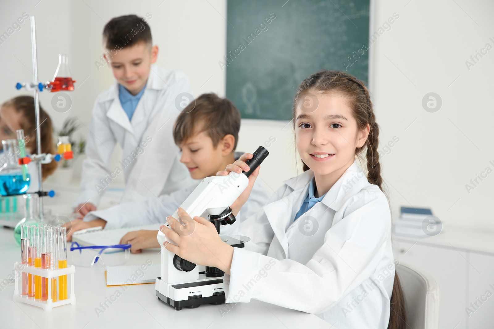 Photo of Schoolgirl with microscope and her classmates at chemistry lesson