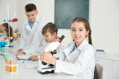 Photo of Schoolgirl with microscope and her classmates at chemistry lesson