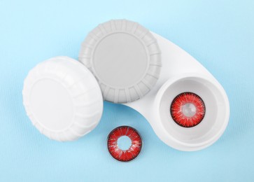 Photo of Case with red contact lenses on light blue background, flat lay