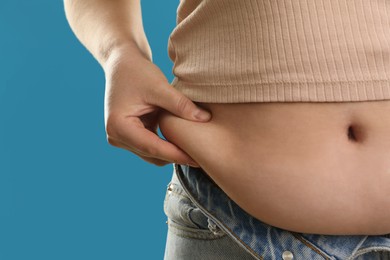 Photo of Woman touching belly fat on light blue background, closeup. Overweight problem