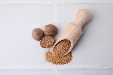 Scoop with grated nutmeg and seeds on white tiled table, flat lay