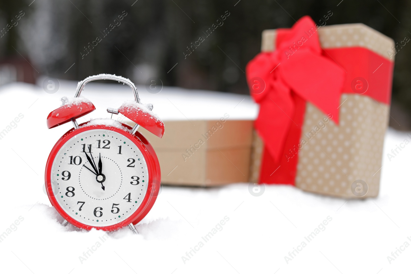 Photo of Red alarm clock with Christmas gifts on white snow outdoors. Space for text