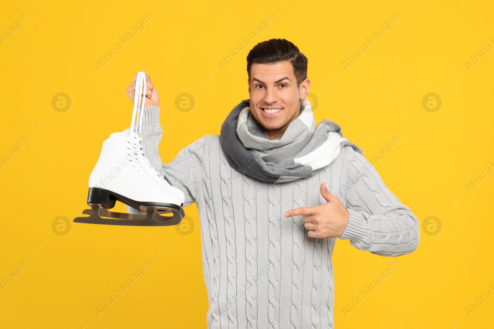 Photo of Happy man with ice skates on yellow background