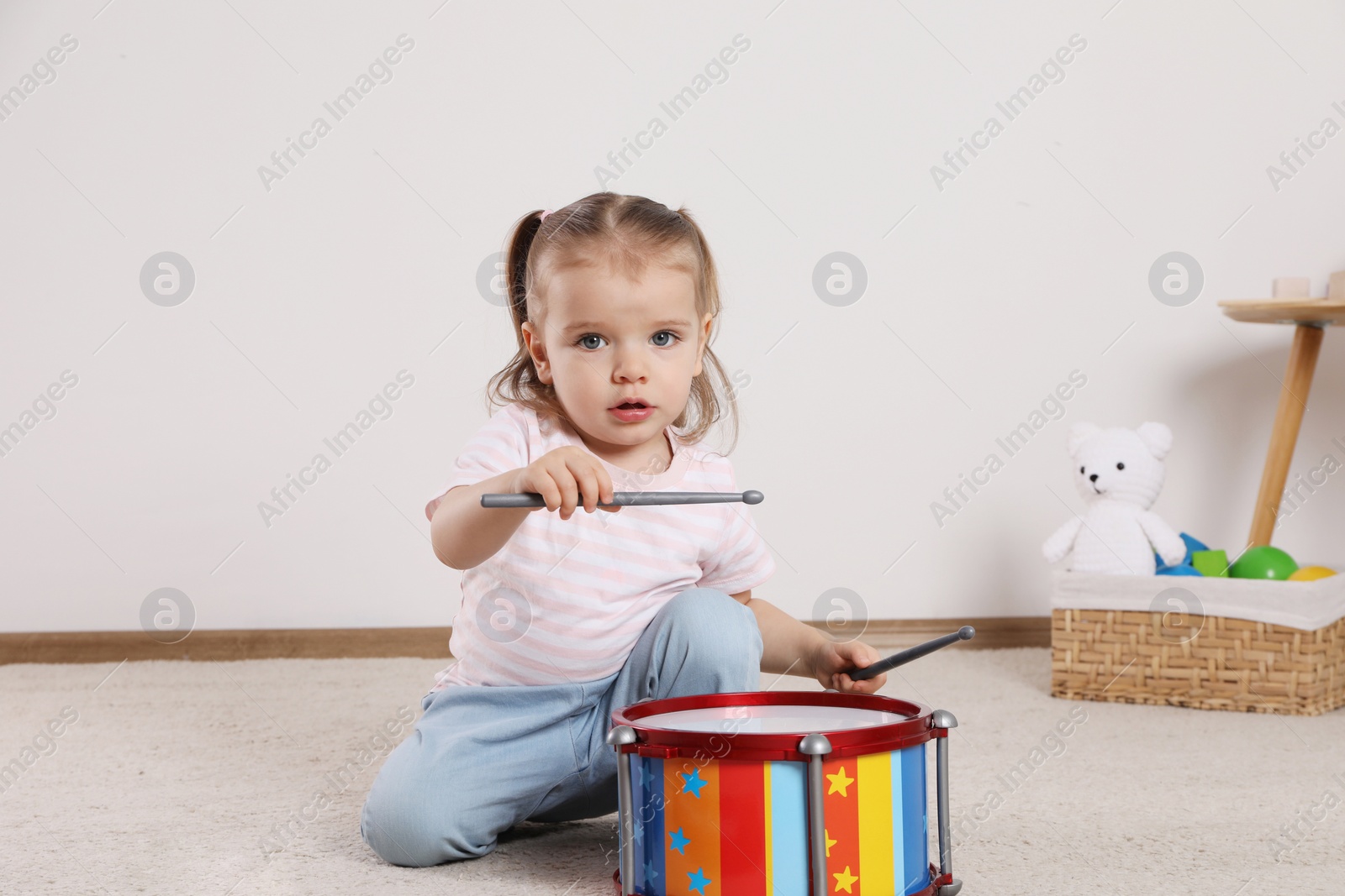 Photo of Cute little girl playing with drum and drumsticks at home