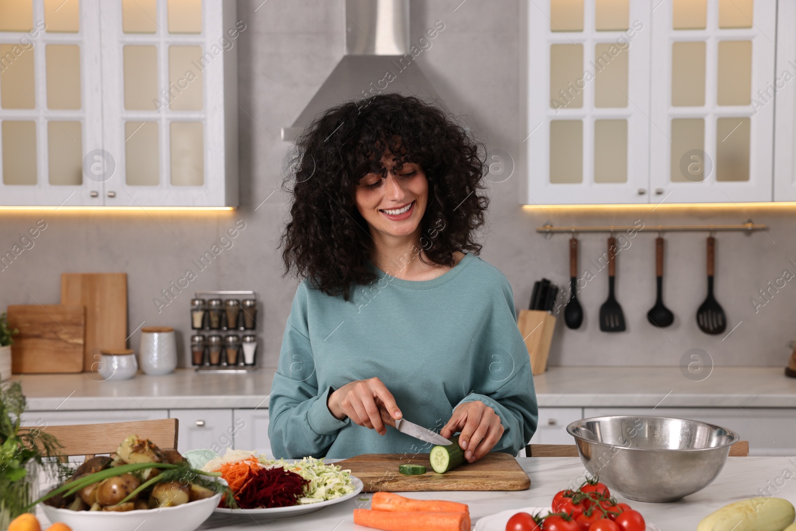 Photo of Woman cooking healthy vegetarian meal at white marble table in kitchen