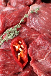 Photo of Pieces of raw beef meat, chili and thyme sprigs as background, closeup