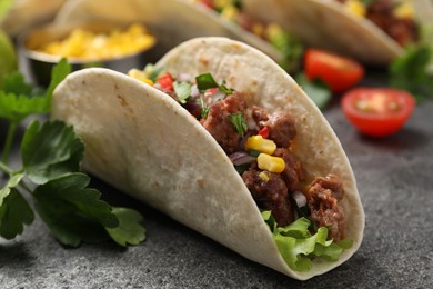 Photo of Delicious taco with meat and vegetables on gray textured table, closeup