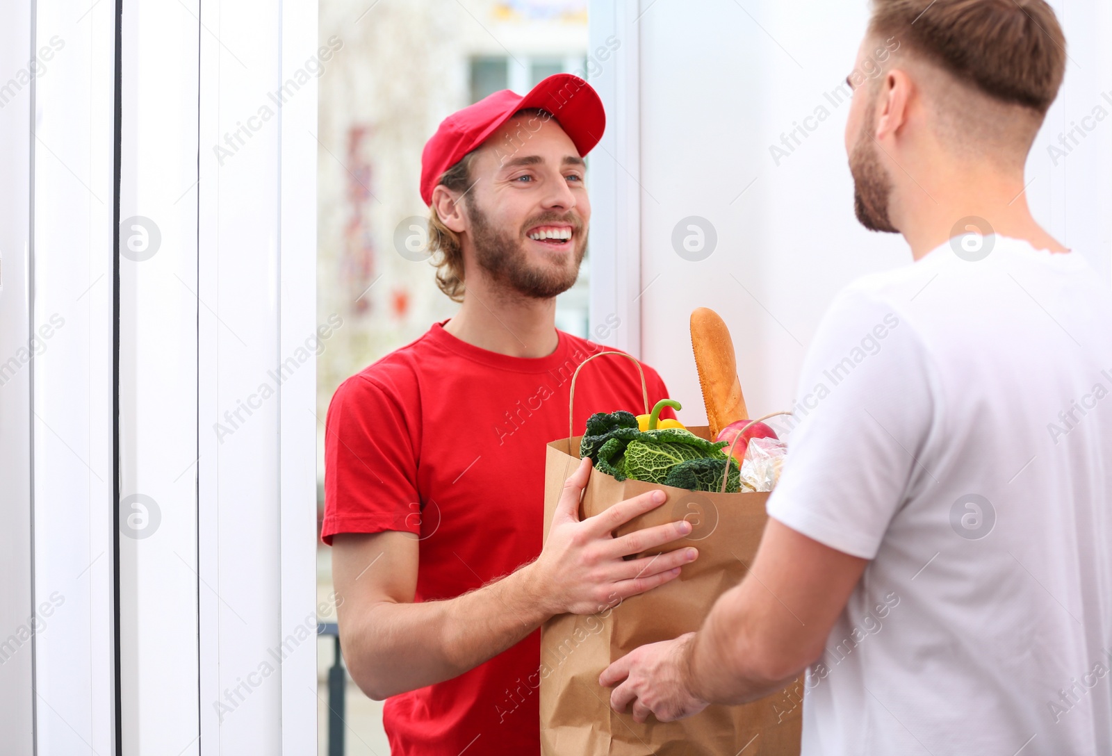 Photo of Courier giving paper bag with products to customer at home. Food delivery service