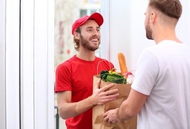 Photo of Courier giving paper bag with products to customer at home. Food delivery service