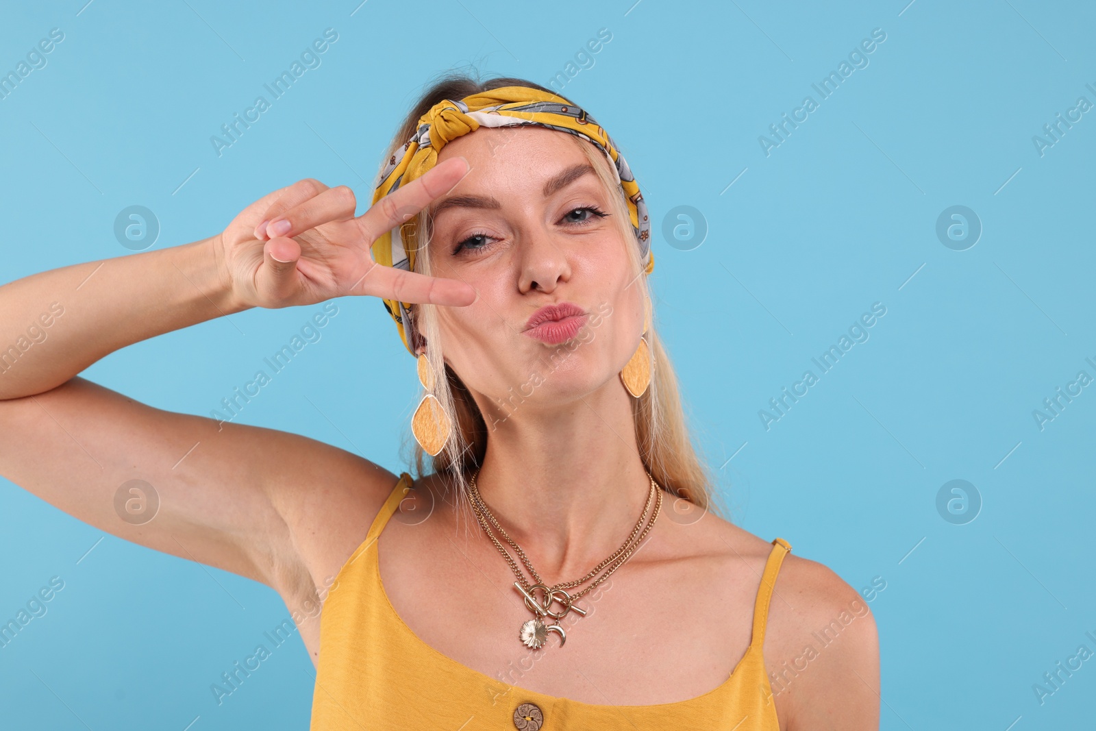 Photo of Portrait of hippie woman showing peace sign on light blue background