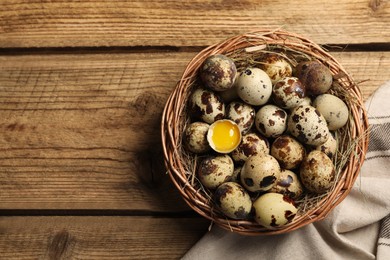 Photo of Wicker bowl with quail eggs and straw on wooden table, top view. Space for text