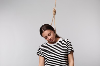 Photo of Depressed woman with rope noose on neck against light grey background