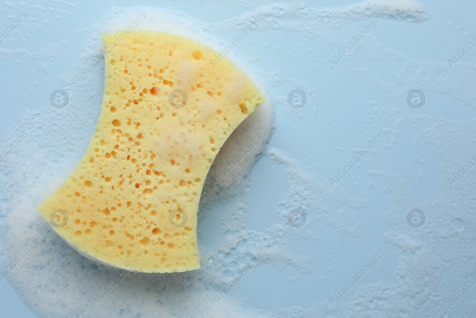 Photo of Yellow sponge with foam on light blue background, top view. Space for text