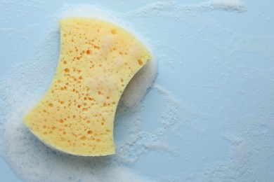 Yellow sponge with foam on light blue background, top view. Space for text