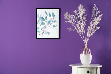 Elegant vase with beautiful branches on table near purple wall