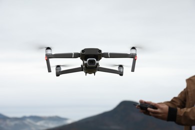 Photo of Man operating modern drone with remote control in mountains