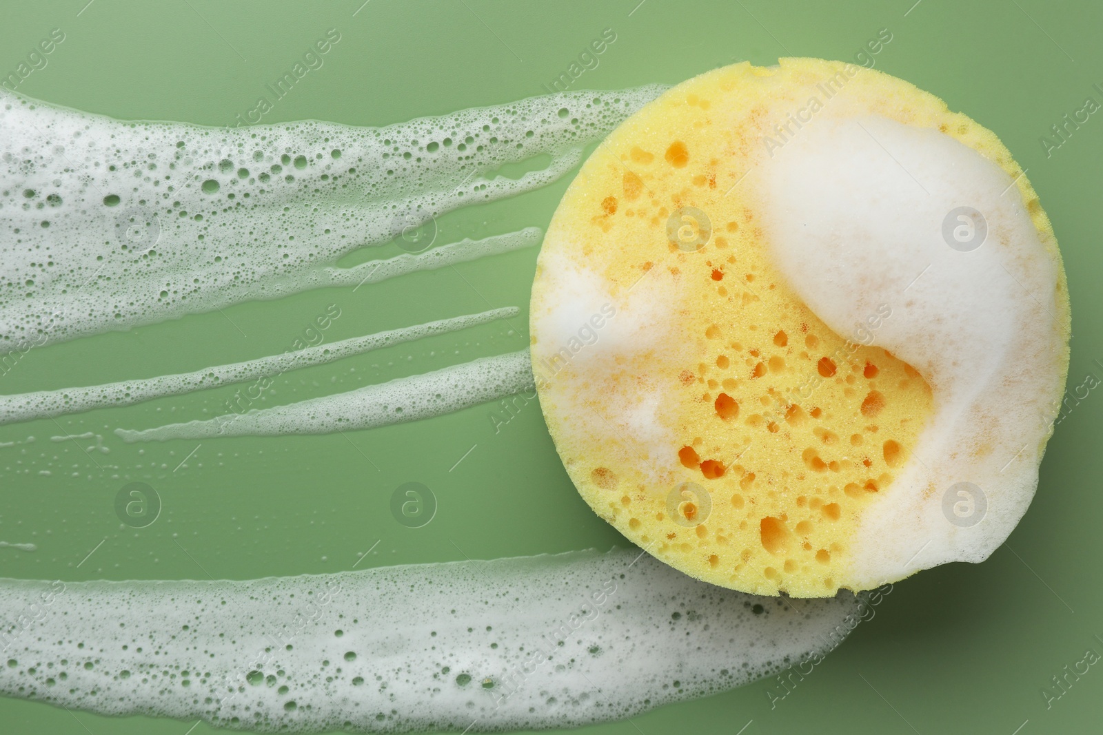 Photo of Yellow sponge with foam on green background, top view