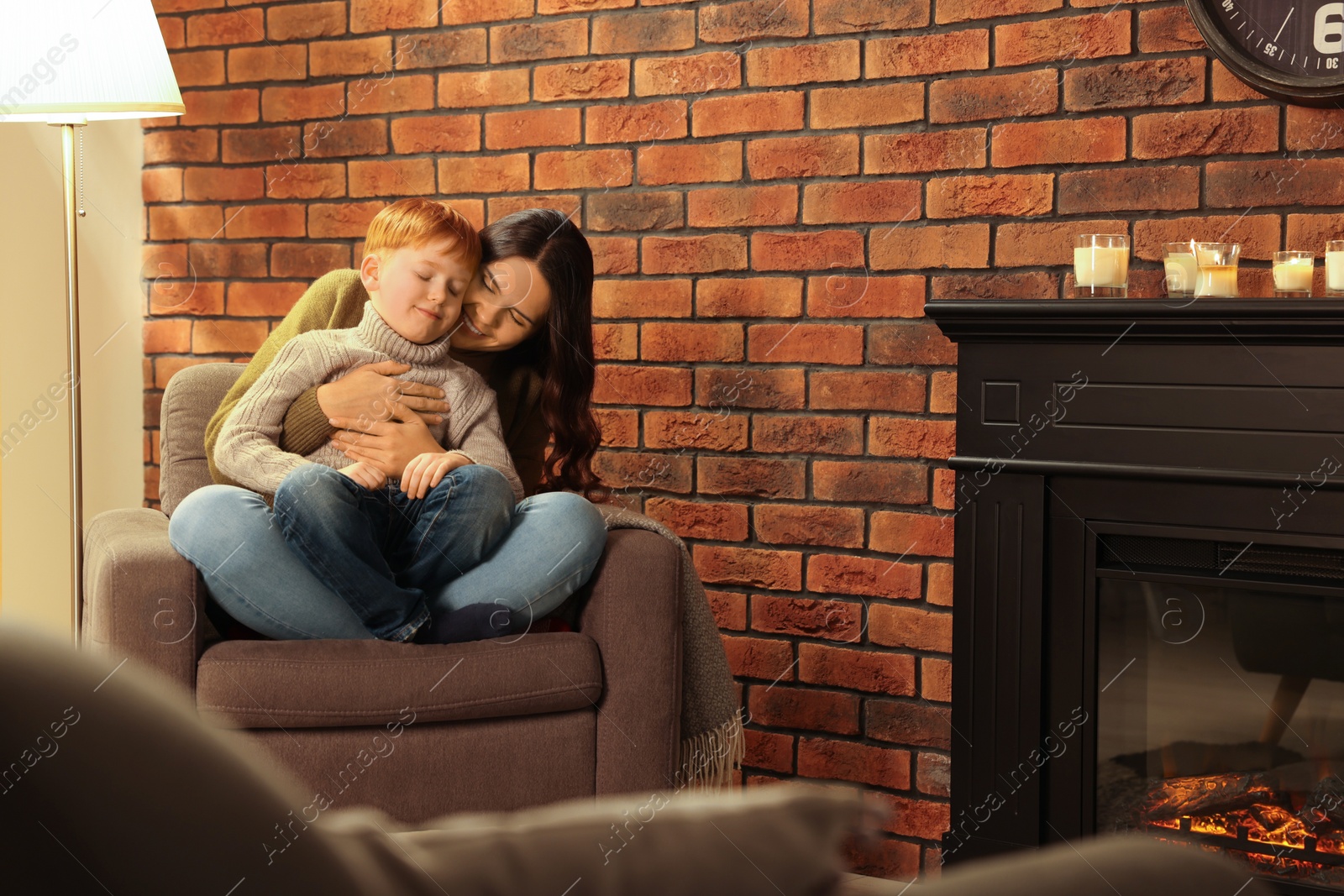 Photo of Happy mother and son hugging near fireplace at home