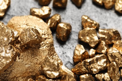 Photo of Pile of shiny gold nuggets on grey table, closeup