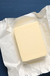 Photo of Block of tasty butter in open foil packaging on blue wooden table, top view