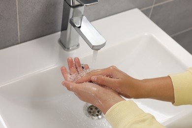 Photo of Woman washing hands with water from tap in bathroom, closeup