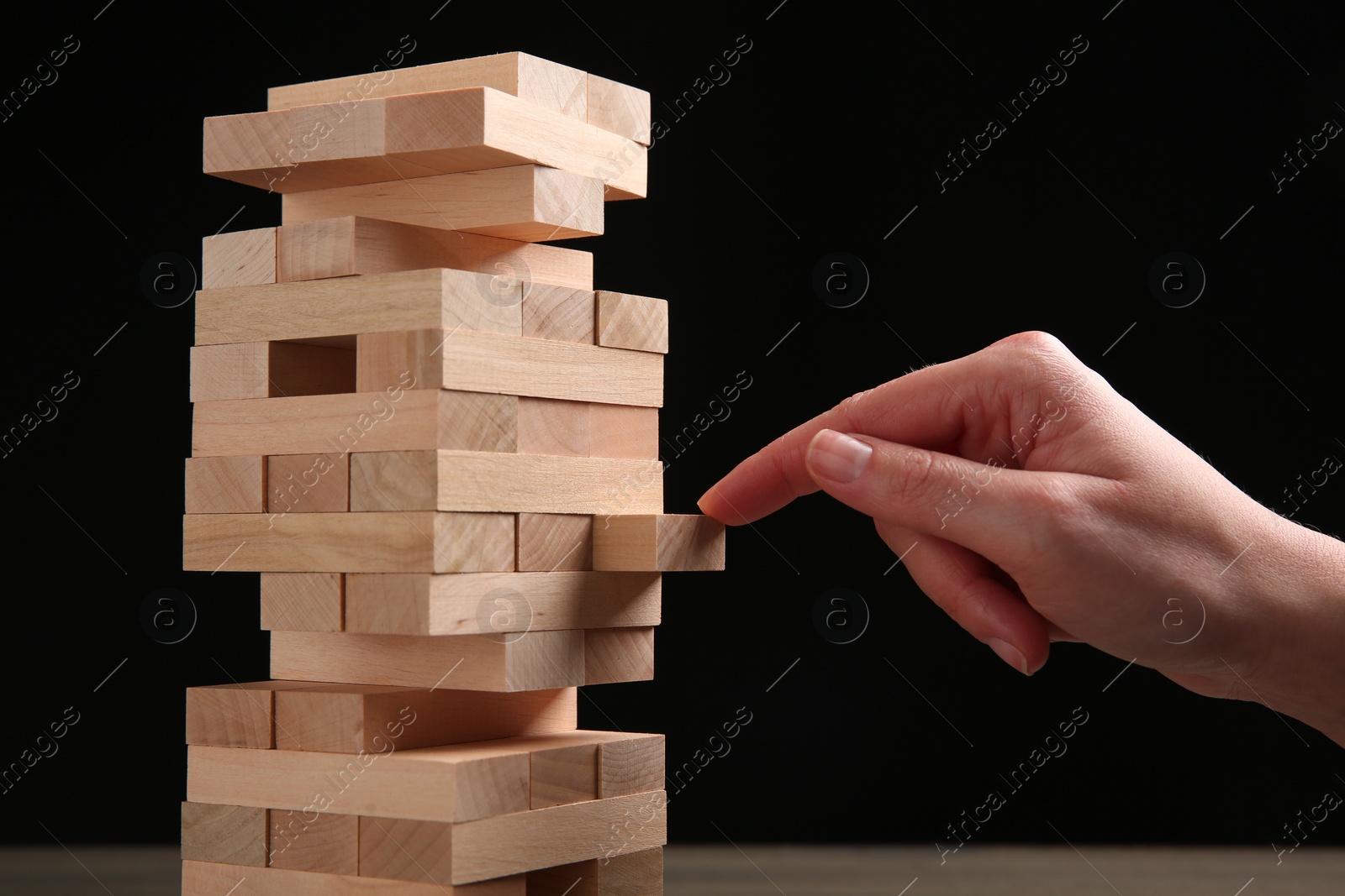 Photo of Woman playing Jenga on black background, closeup