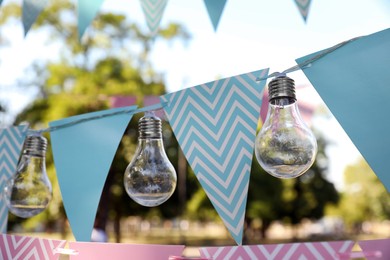 Photo of Colorful bunting flags with light bulbs in park. Party decor
