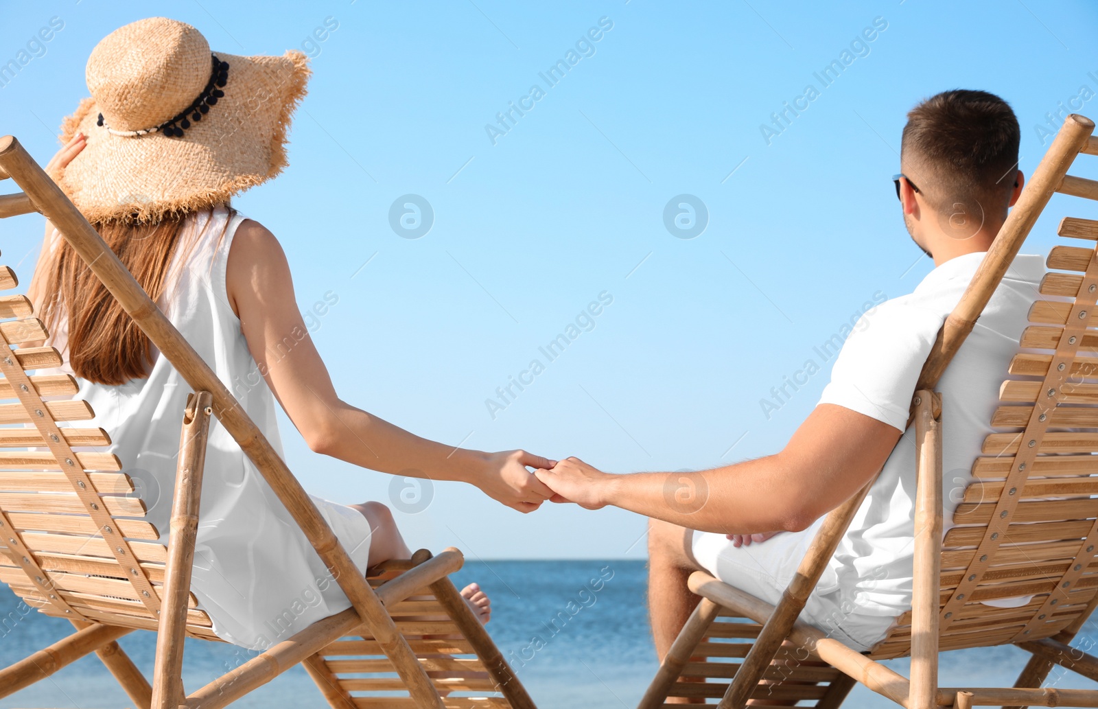 Photo of Young couple relaxing in deck chairs on beach