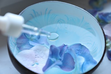 Photo of Dripping essential oil from pipette into bowl with water and flowers, closeup