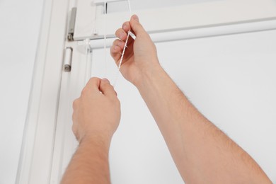 Photo of Man opening roller window blind indoors, closeup