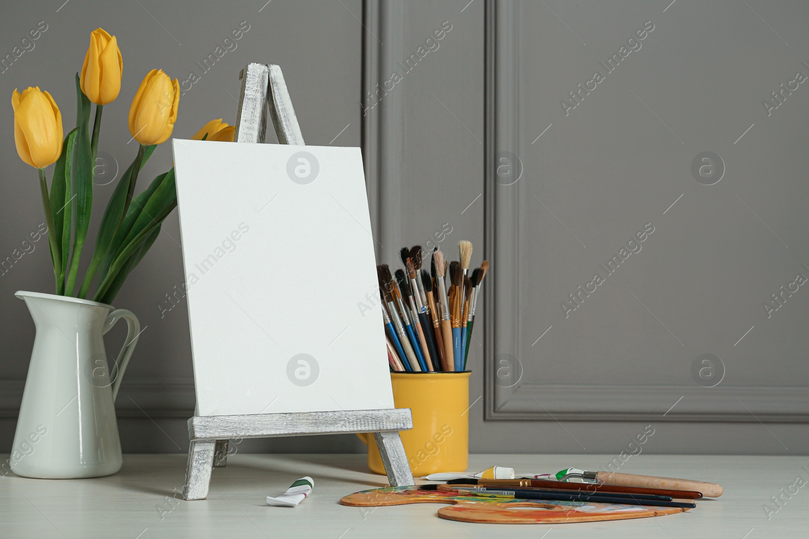 Photo of Easel with blank canvas, brushes, paints and palette. Space for text