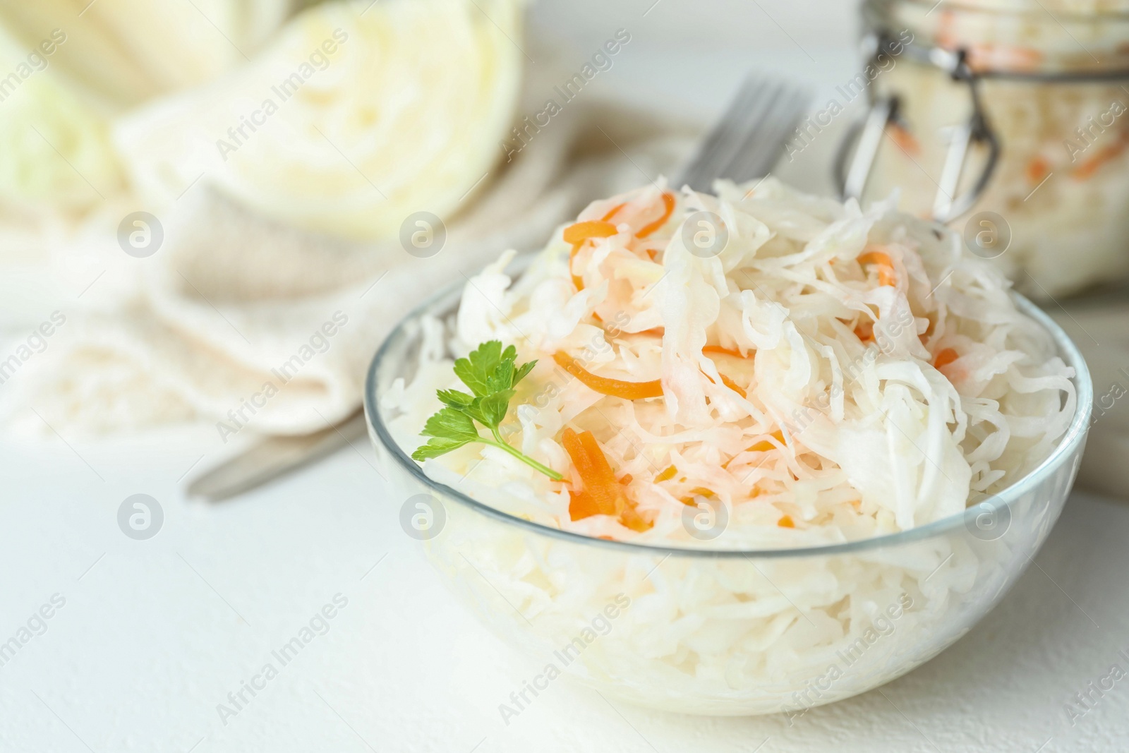 Photo of Glass bowl of tasty fermented cabbage on white table, closeup