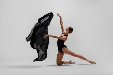 Photo of Graceful young ballerina practicing dance moves with black veil on white background