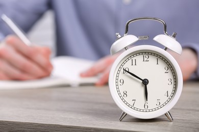 Photo of White alarm clock and man working at wooden table, closeup. Space for text