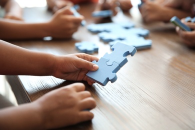 Photo of Little children playing with puzzle at table, focus on hands. Unity concept