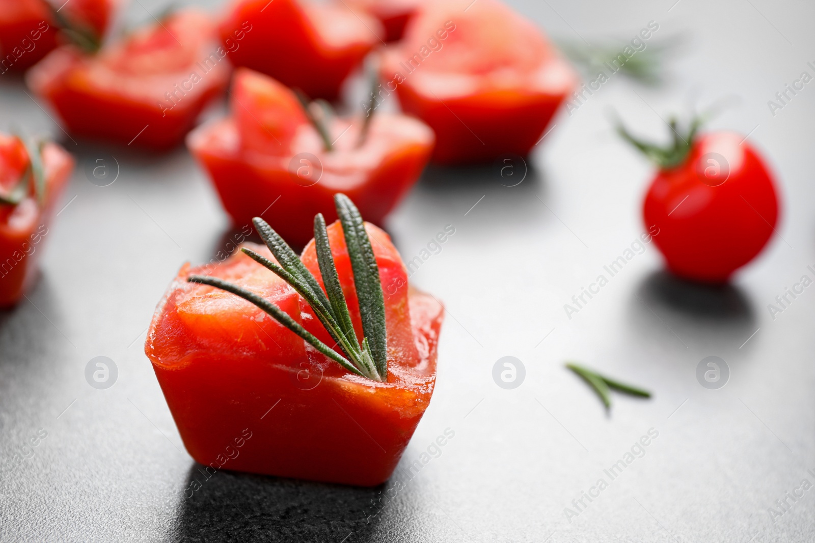 Photo of Ice cubes with tomatoes and rosemary on grey table, closeup