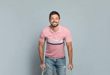Portrait of happy man with crutches on grey background