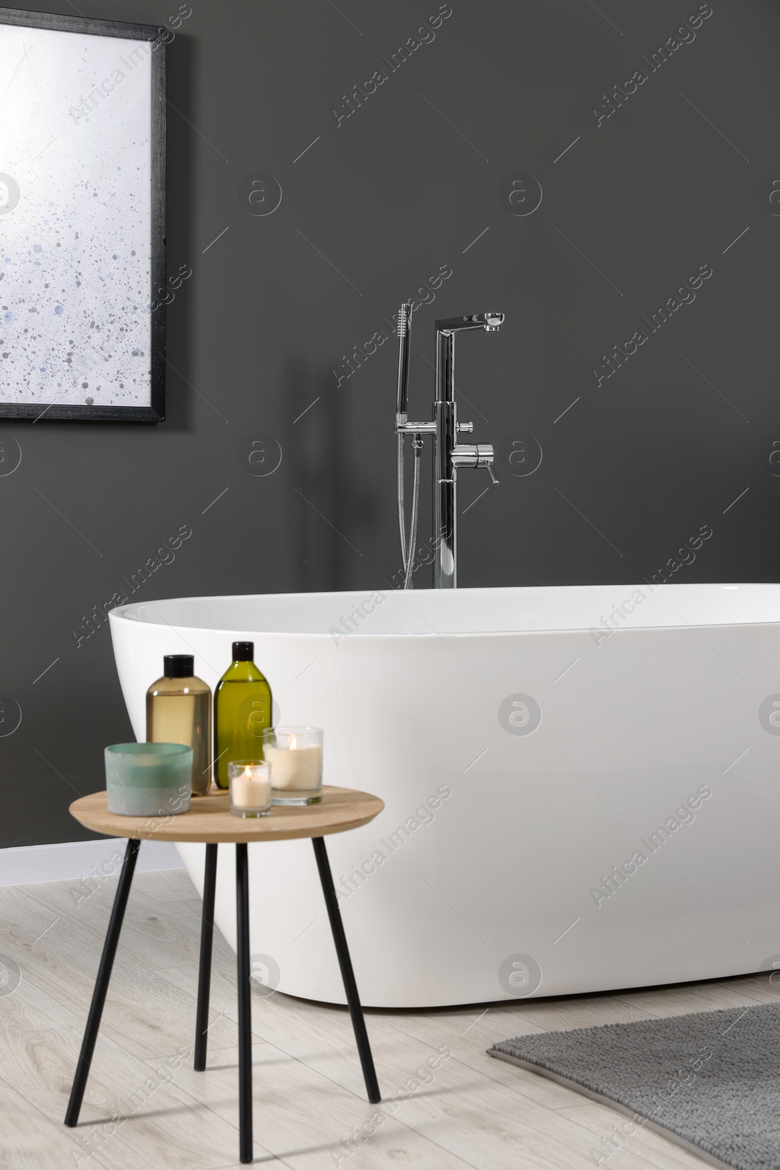 Photo of Stylish bathroom interior with ceramic tub and care products on coffee table