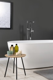 Photo of Stylish bathroom interior with ceramic tub and care products on coffee table