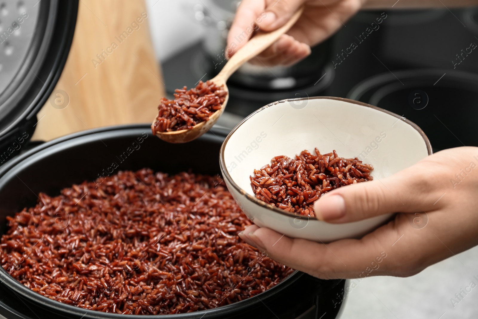 Photo of Woman putting brown rice into bowl from multi cooker in kitchen, closeup