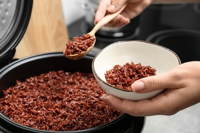 Woman putting brown rice into bowl from multi cooker in kitchen, closeup