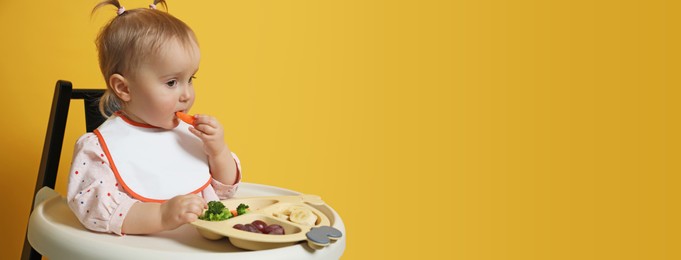 Image of Cute little baby wearing bib while eating on yellow background, space for text. Banner design