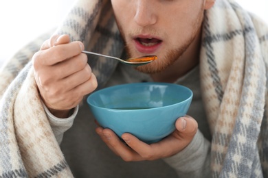 Photo of Sick young man eating soup to cure flu, closeup