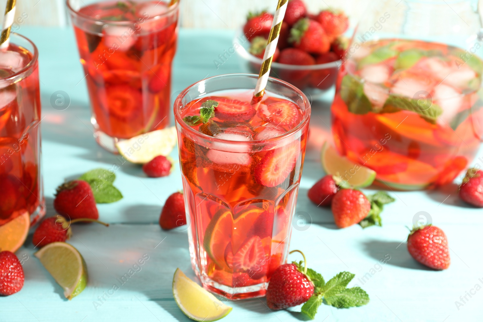 Photo of Refreshing drink with strawberry and lime on light blue wooden table